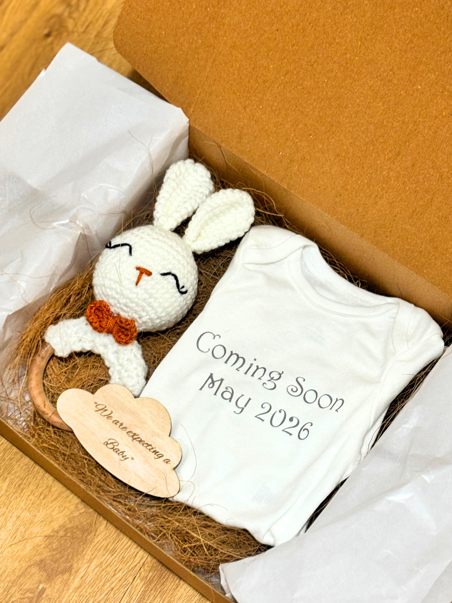 Baby shower gift set with white bunny toy, baby onesie, and 'Coming Soon' sign in a box.