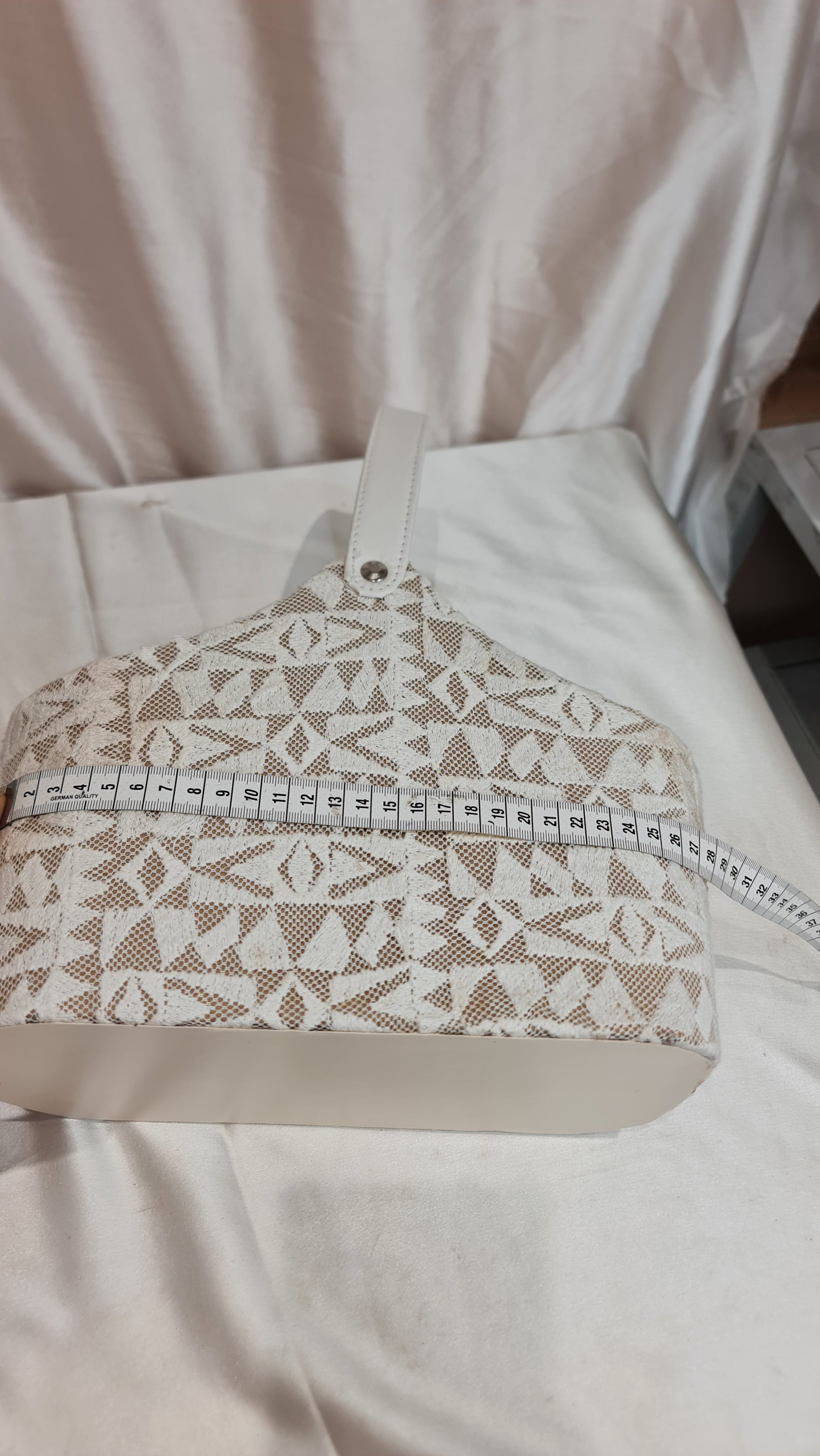 Close-up of a white garment with a patterned pocket and zipper on a plain background