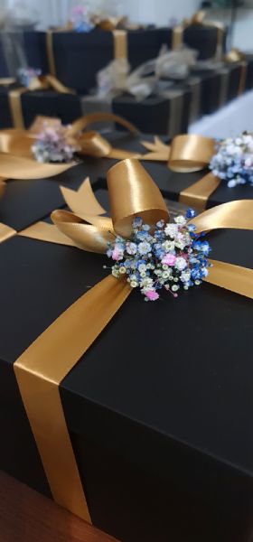 Black gift box with gold ribbon and decorative flowers on a blurred background