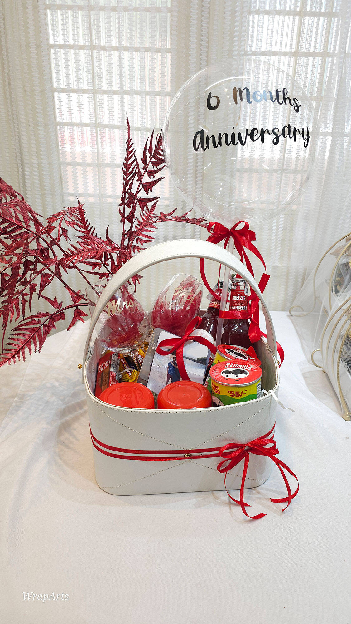 Gift basket with drinks and snacks on a white surface with a decorative background