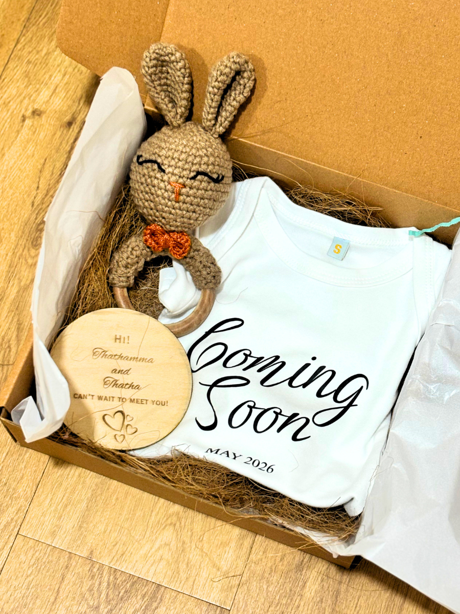 Gift set with a crochet bunny, wooden plaque, and 'Coming Soon' shirt in a box.