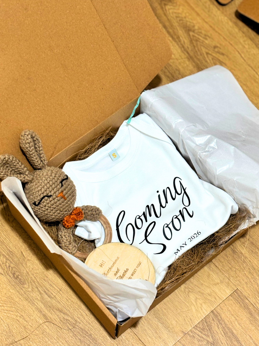 Box with a crochet bunny, baby shower pillow, and 'Coming Soon' sign on a wooden floor.
