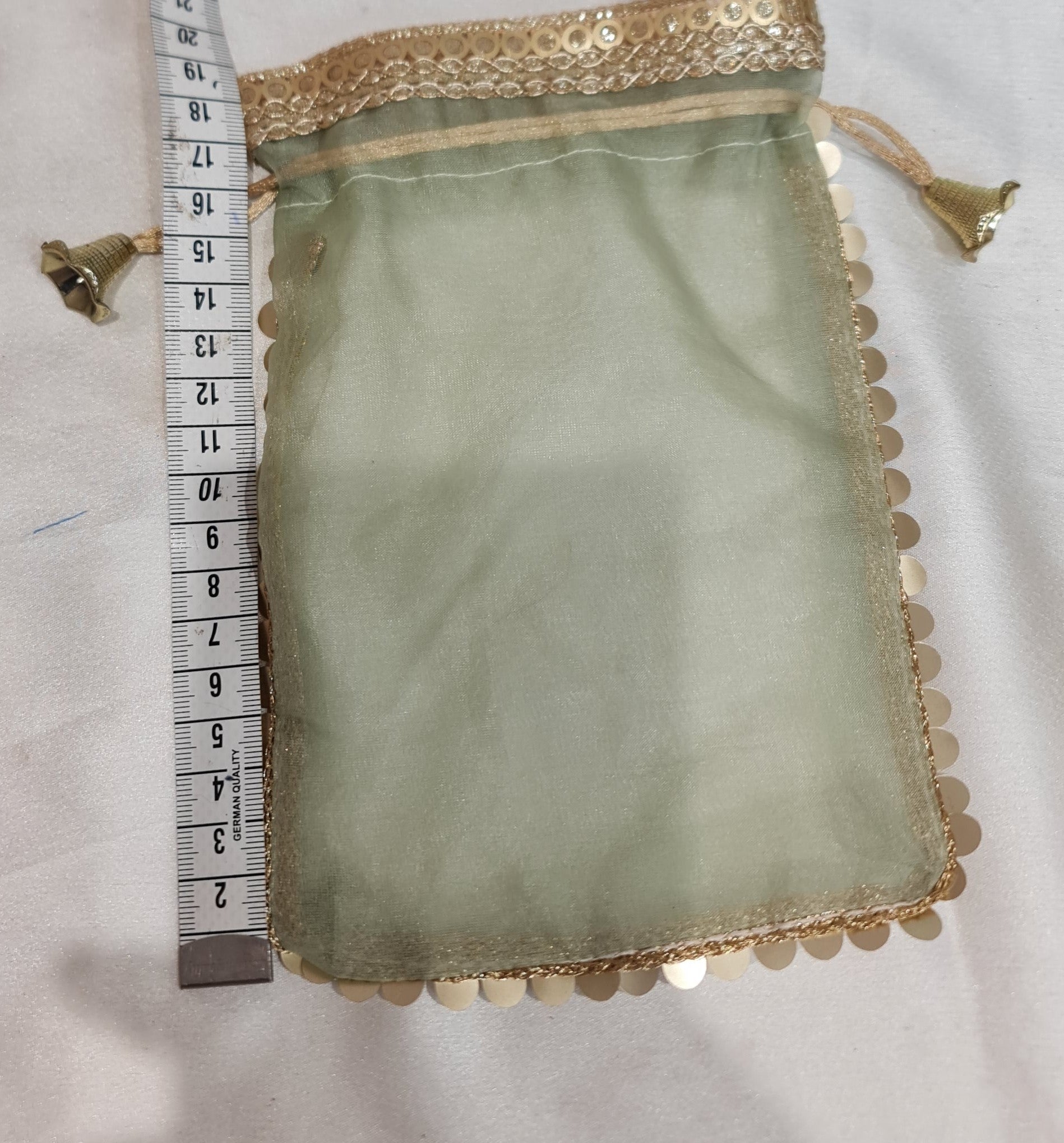Green fabric pouch with gold trim and a measuring tape for scale on a light gray background