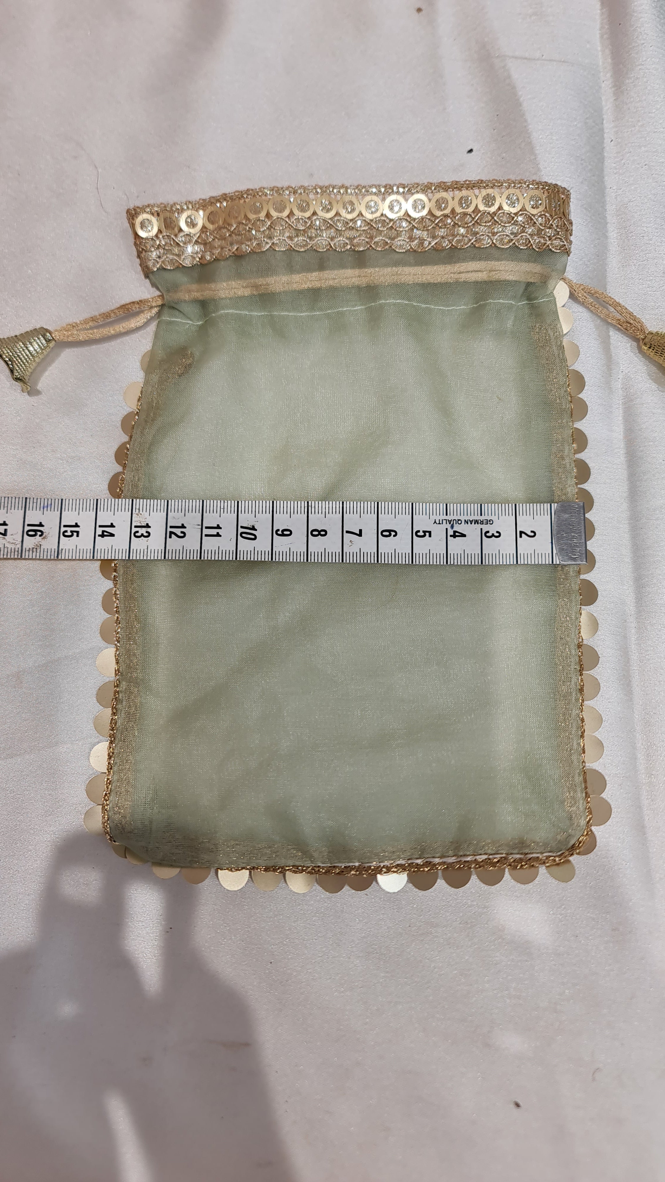 Small green fabric pouch with lace trim and a measuring tape for scale on a white background