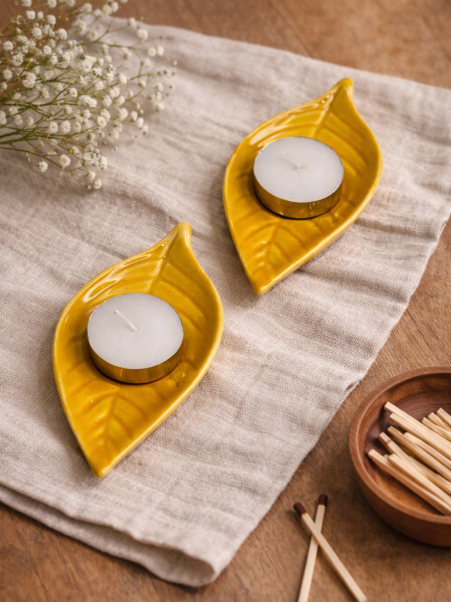 Two yellow leaf-shaped candle holders with white candles on a beige cloth.