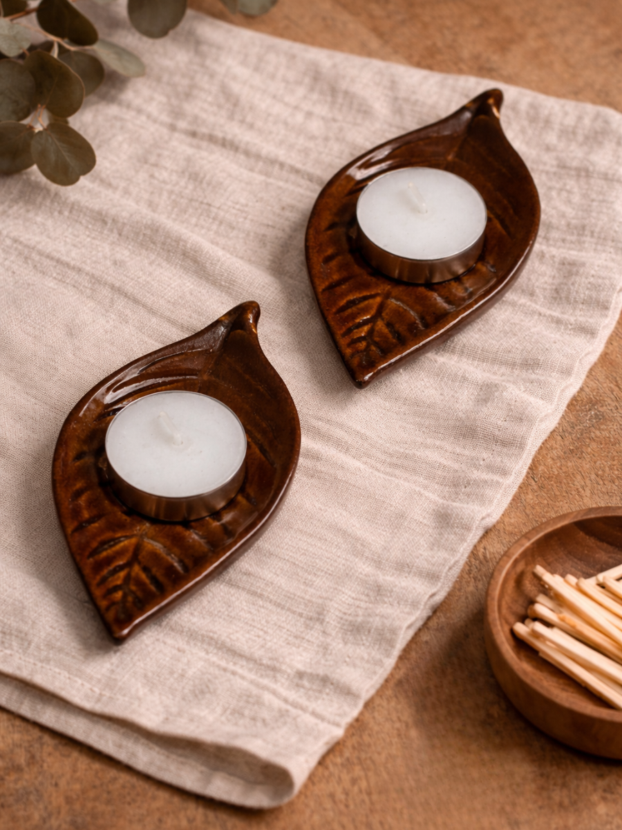 Two leaf-shaped candle holders with candles on a textured fabric surface.