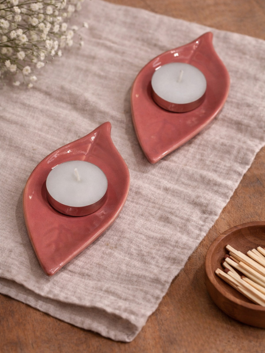 Two pink ceramic candle holders with white candles on a textured surface.