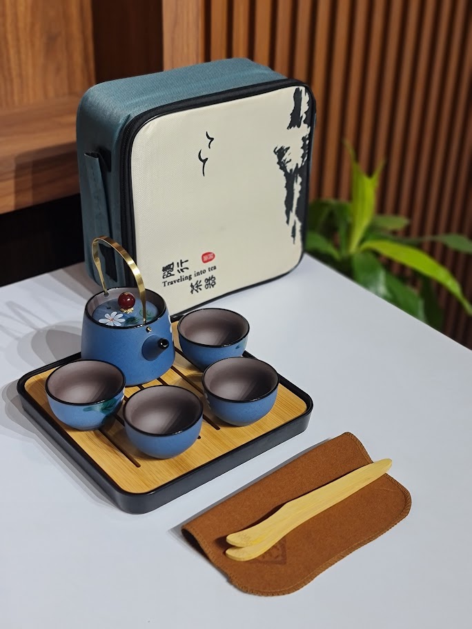 Tea set with blue teapot and cups on a wooden tray, accompanied by a carrying case.