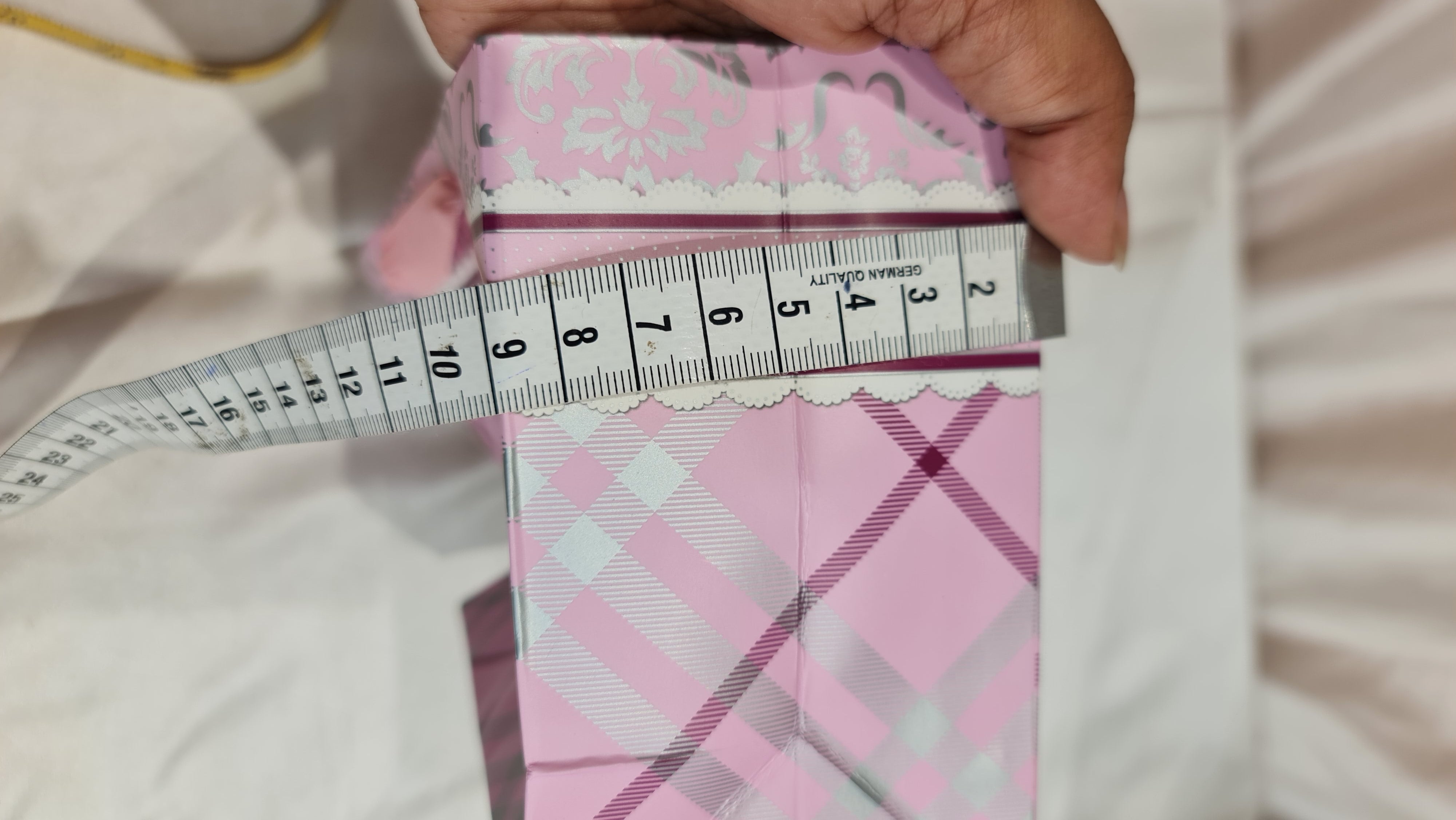 Pink and white checkered fabric with a measuring tape held by a hand on a light background