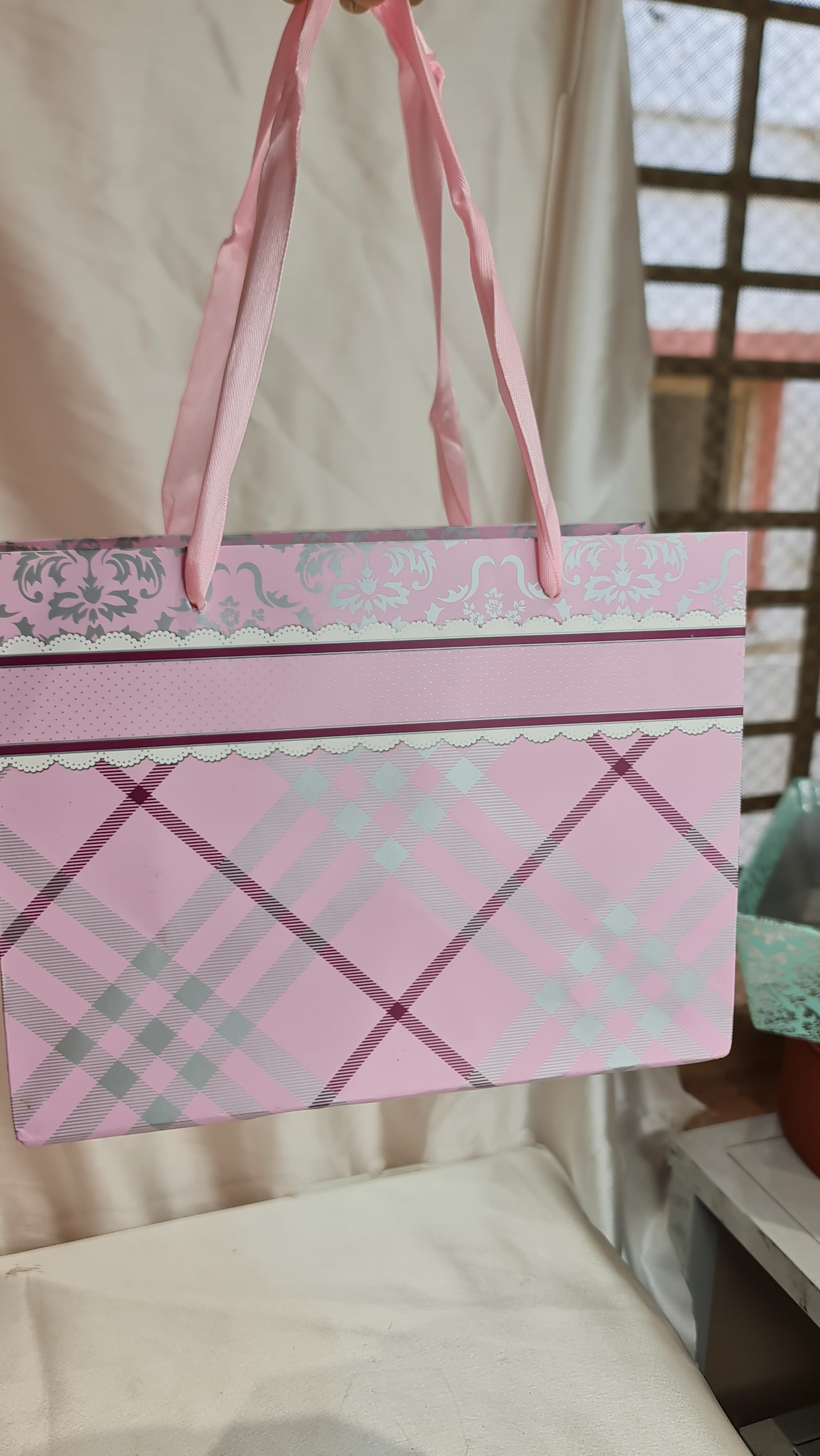 Pink and white checkered box with decorative ribbon on a bed