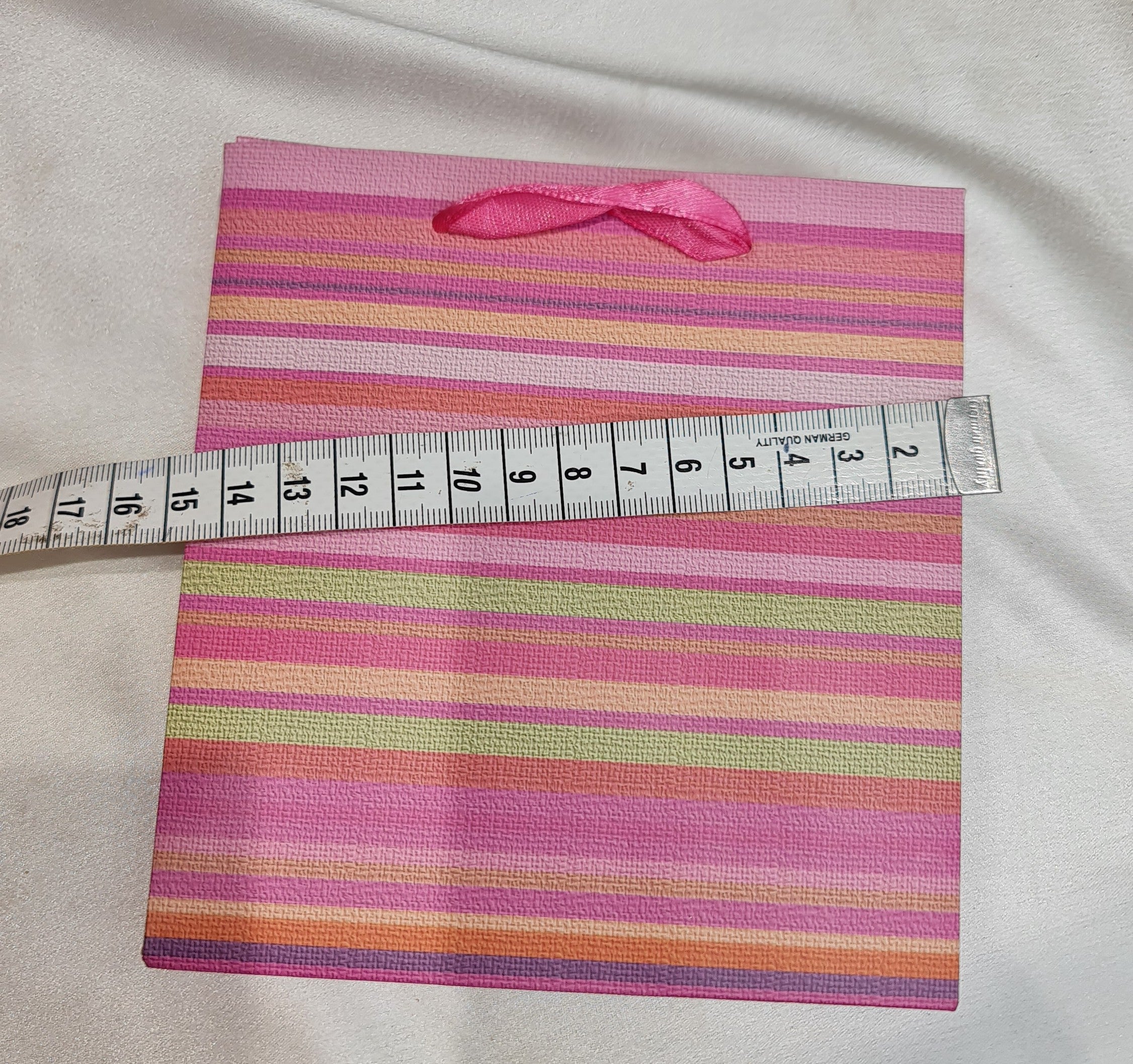 Striped fabric with a pink ribbon and a measuring tape on a light gray background