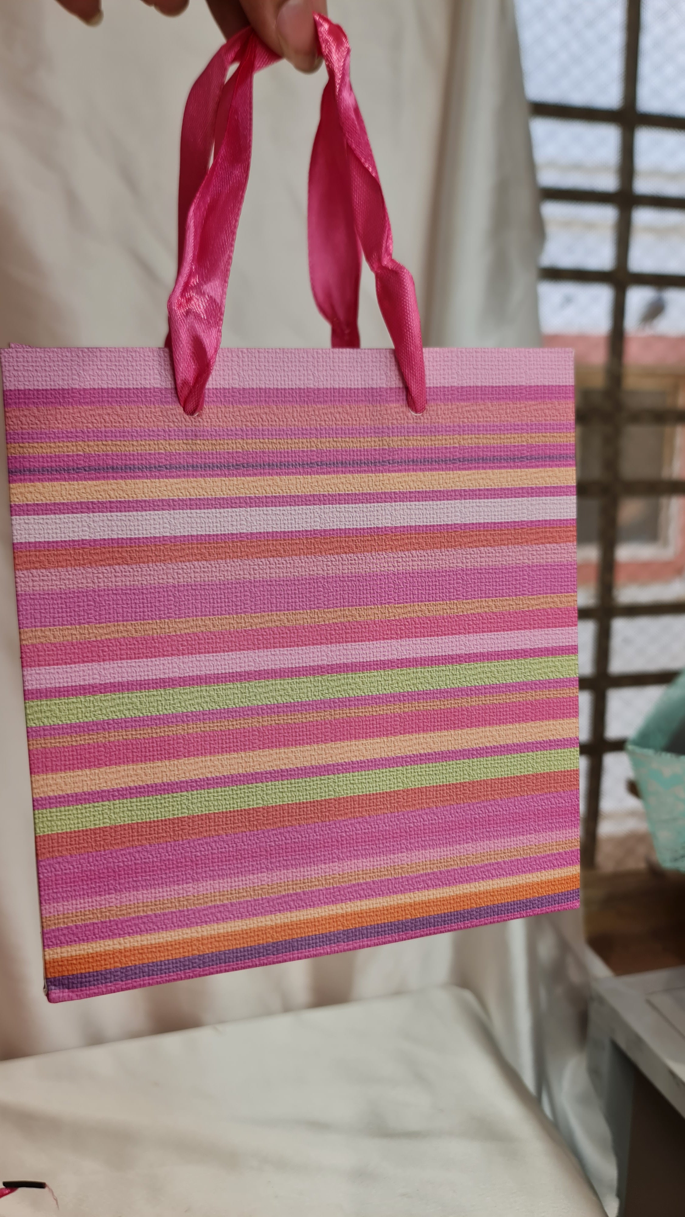 Colorful striped fabric with a pink ribbon held by a hand on a blurred background