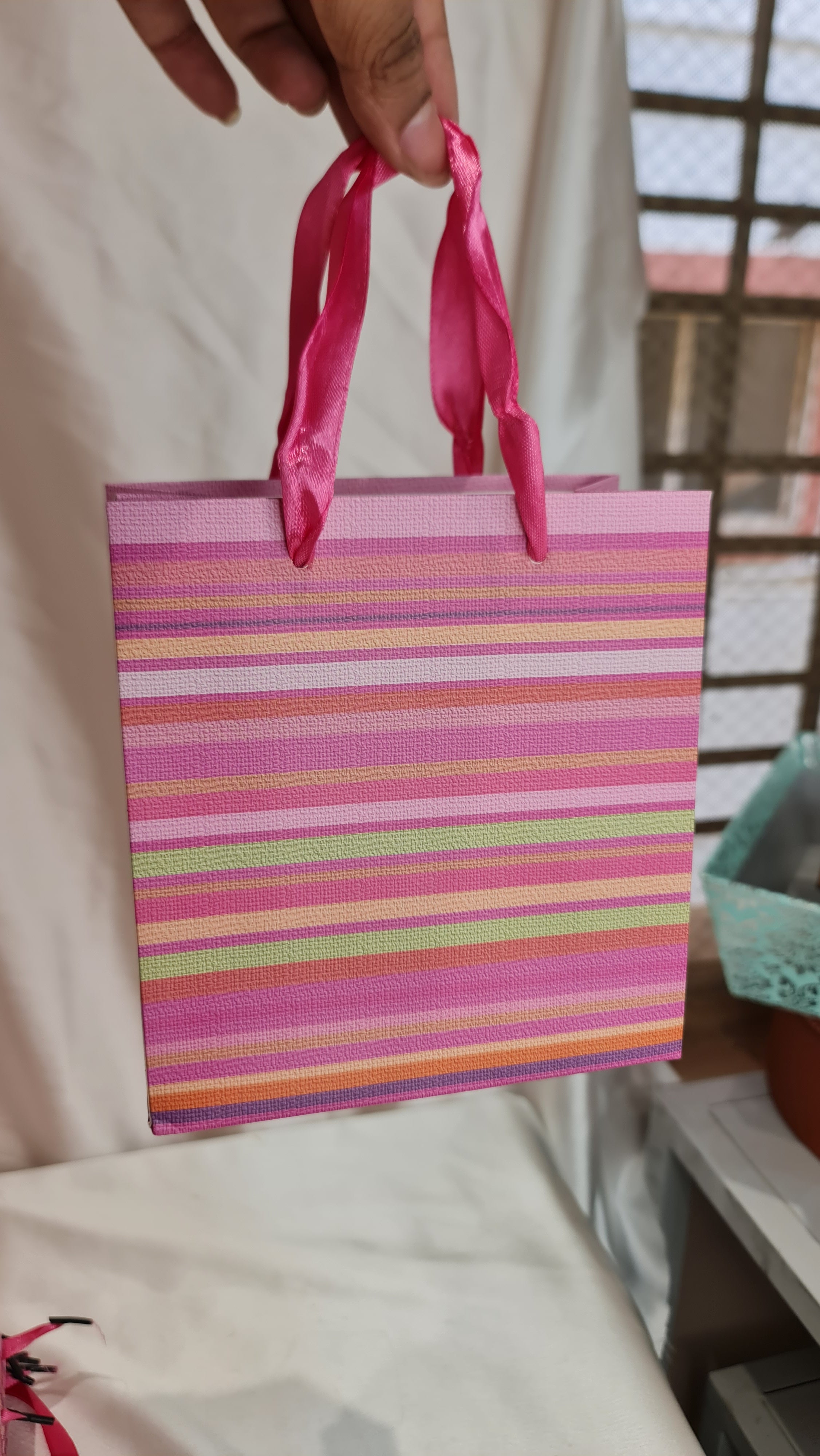 Striped bag with a pink handle held by a hand on a bed