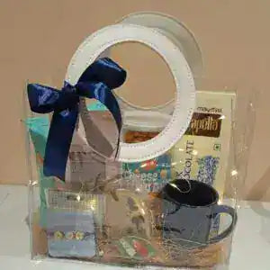 Gift basket with a blue ribbon, including snacks and a mug, on a beige background.
