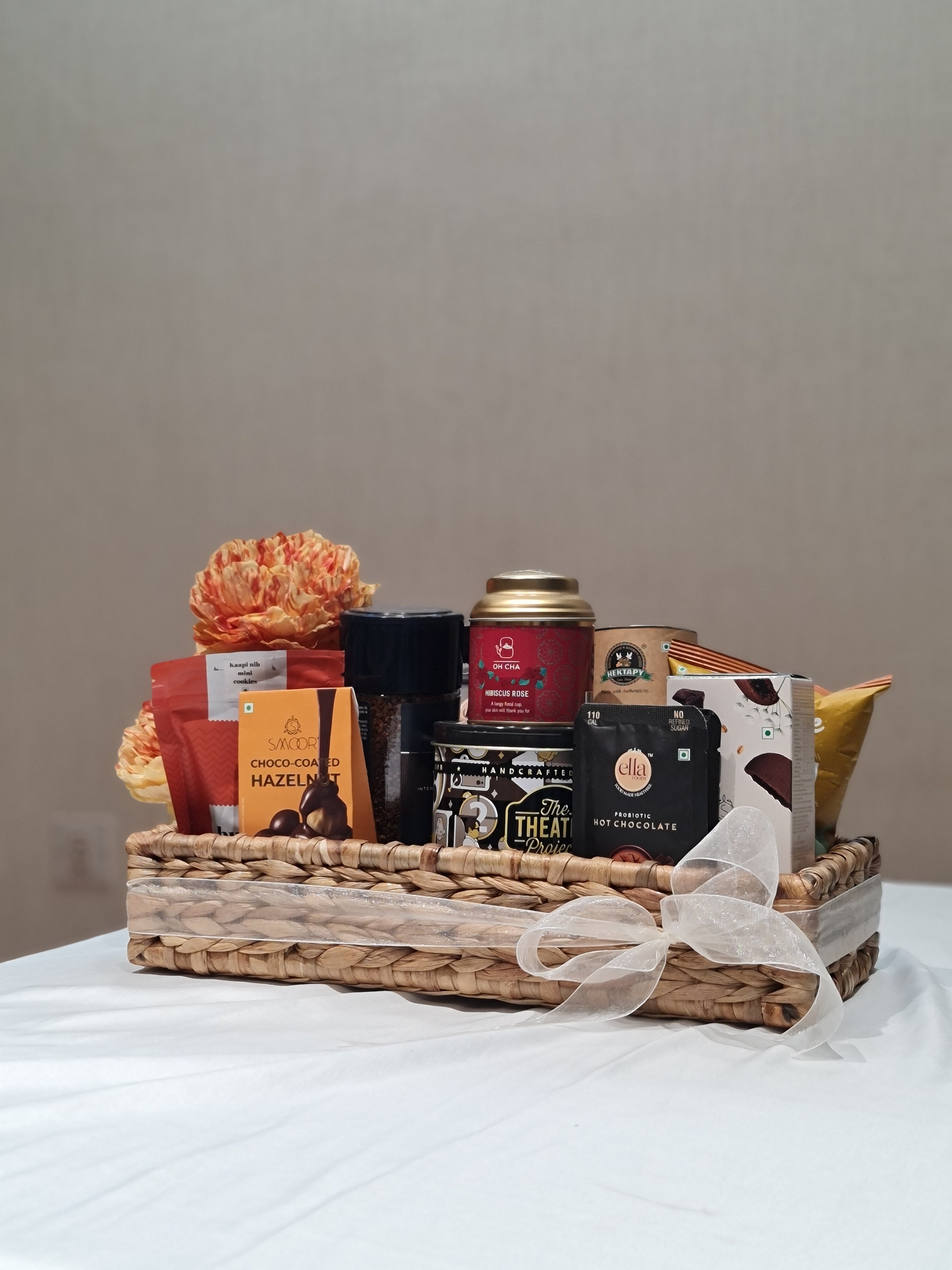 Wicker gift basket with snacks and drinks on a white surface