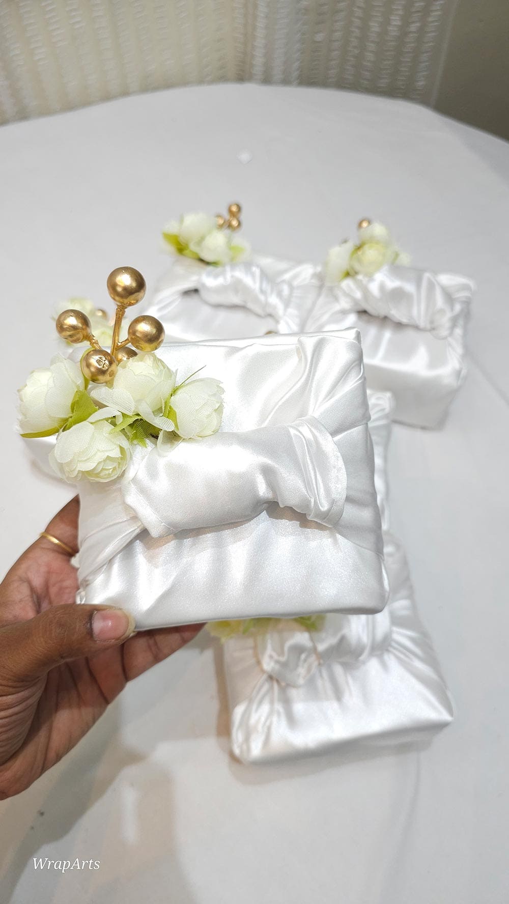 White satin box with decorative flowers held by a hand on a white surface