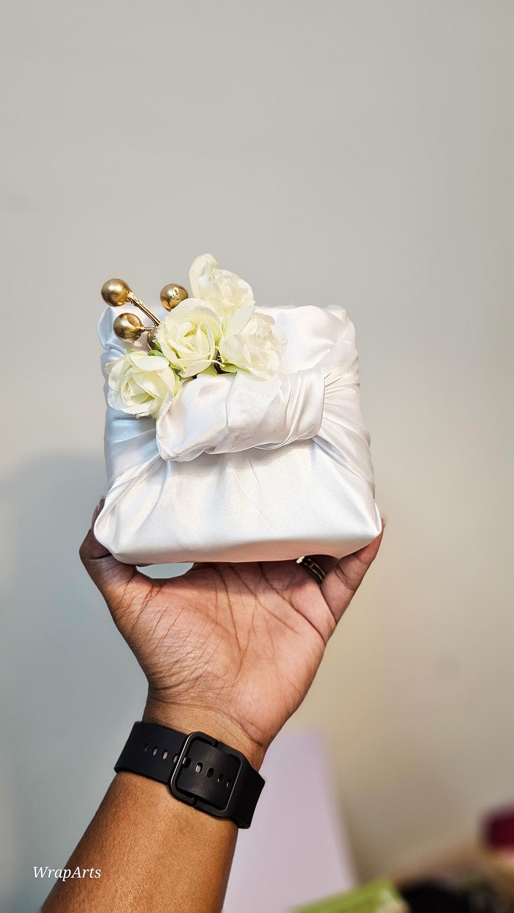 White fabric pouch with flowers held by a hand against a neutral background