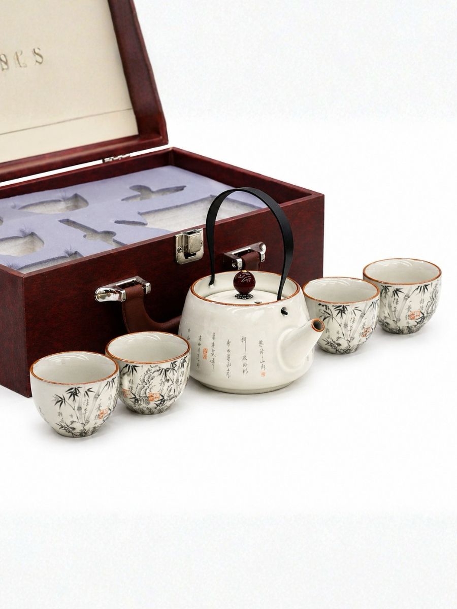 Tea set with teapot and cups in front of an open wooden box on a white background