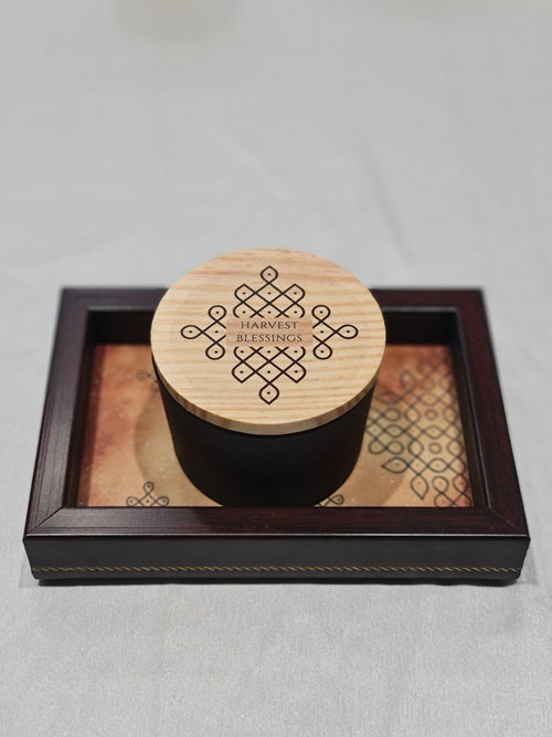 Black container with wooden lid on a decorative tray against a light gray background