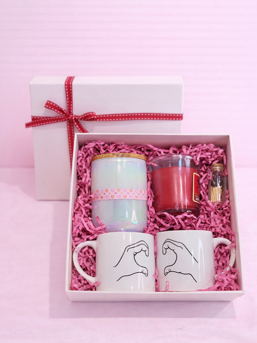 Gift set with mugs, a candle, and a bottle in a box on a pink background