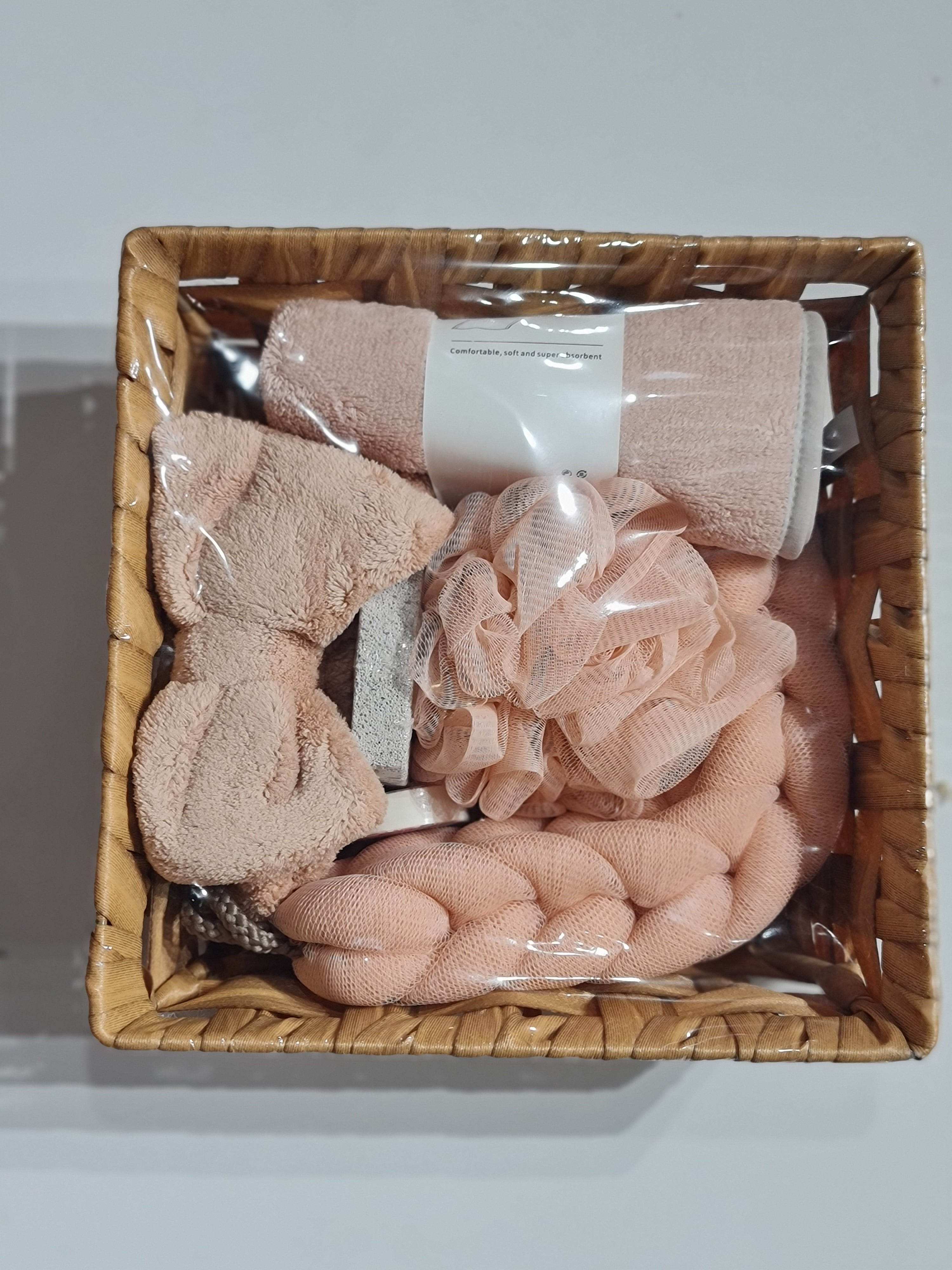 Set of bath products including towels and loofahs in a woven basket on a white background