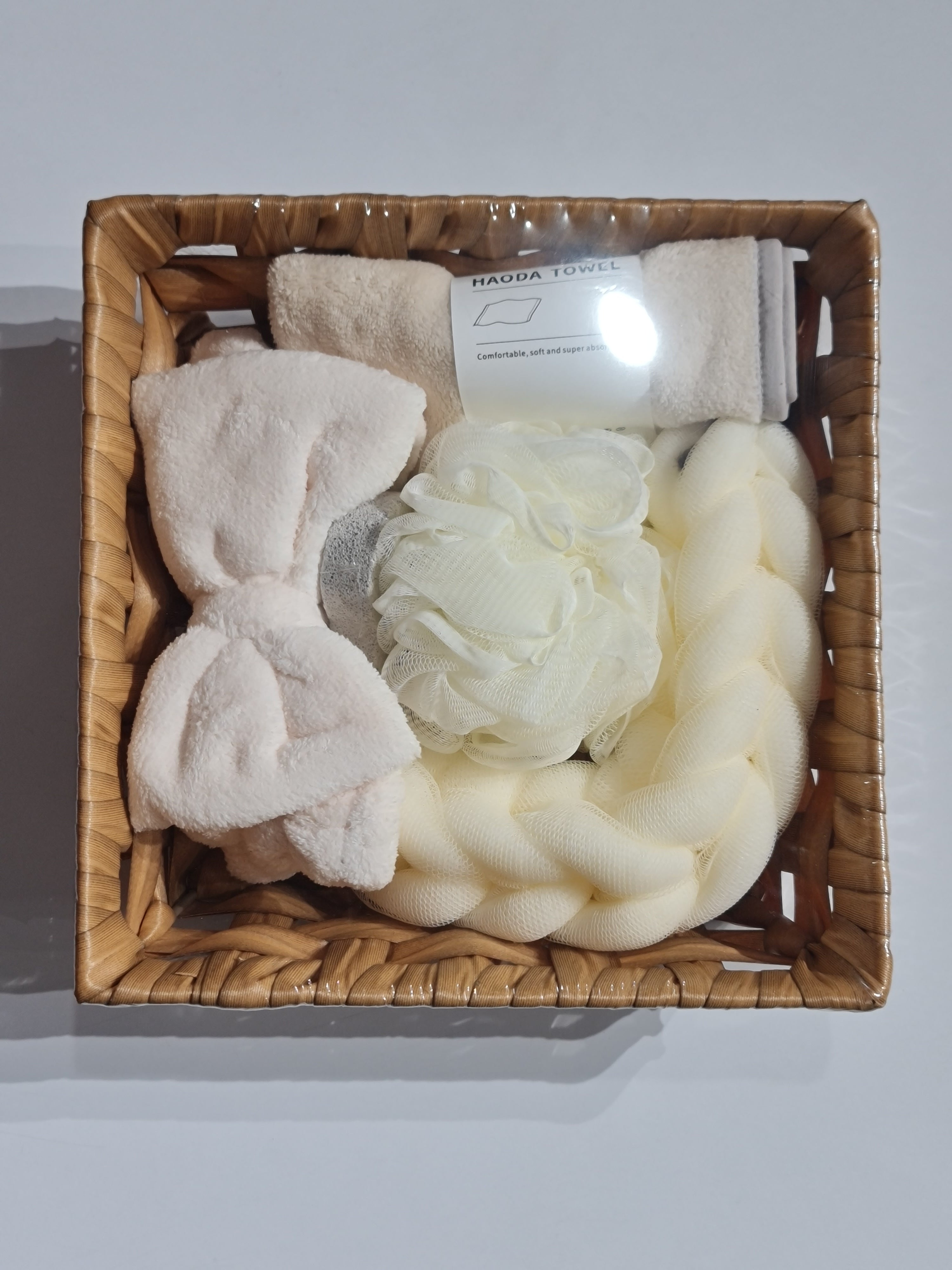 Basket with bath products including loofahs and towels on a light gray background
