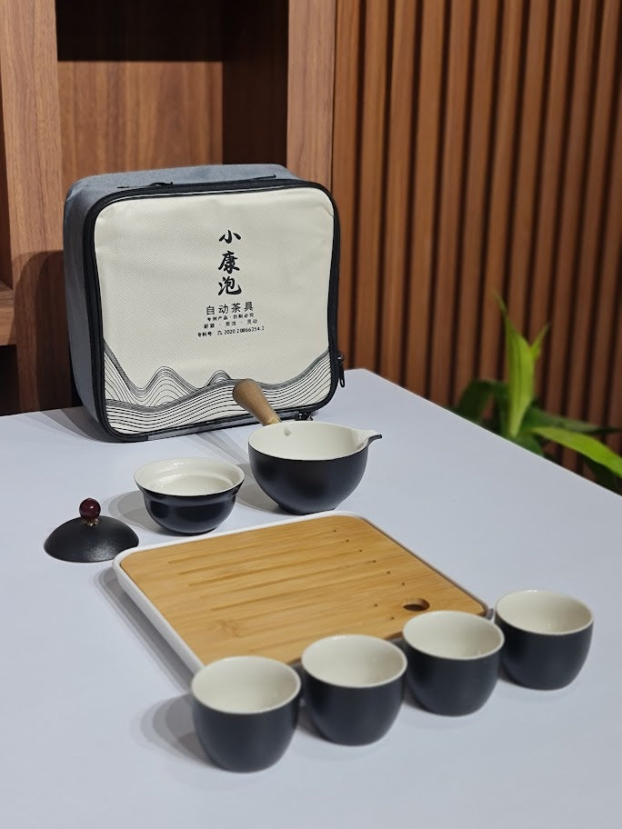 Tea set with black teacups, a wooden tray, and a carrying case on a light surface.