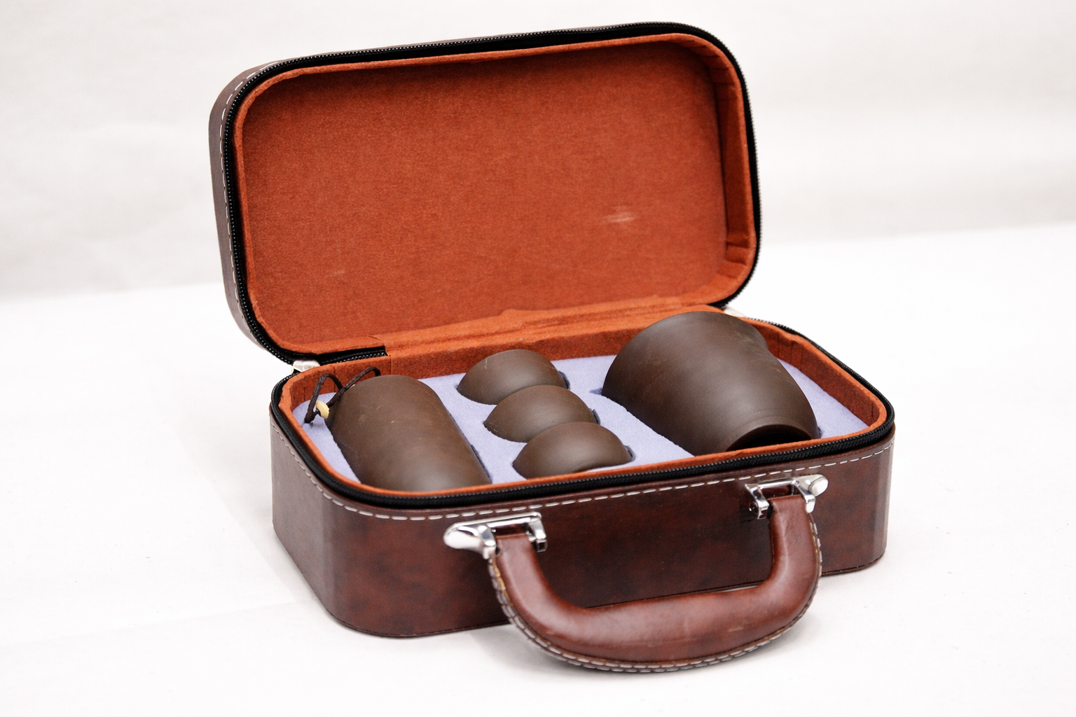 Brown leather case with open lid displaying four brown cups on a white background