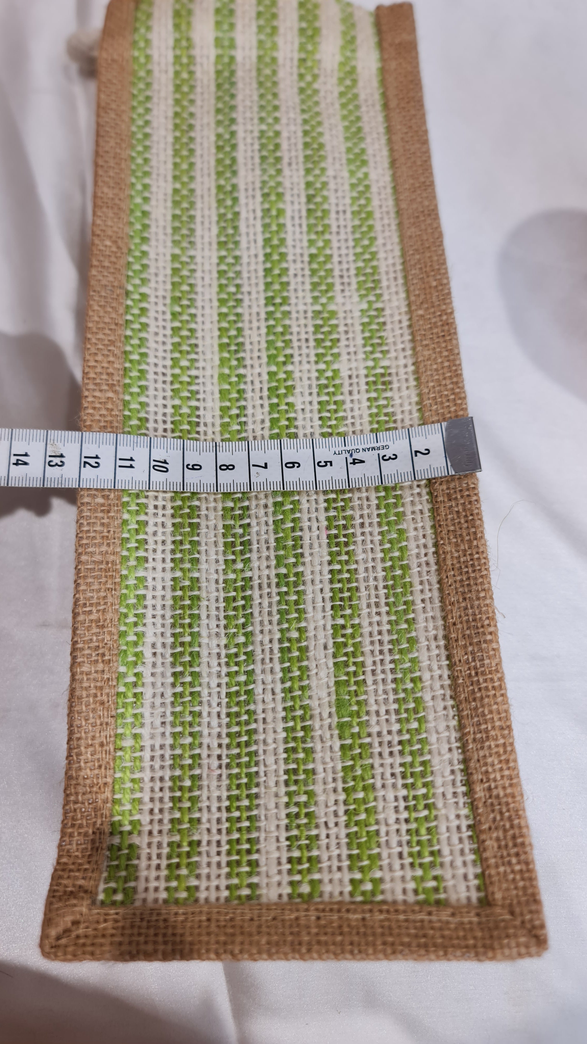 Fabric strip with green and white pattern and brown border, measured with a tape measure on a white background.