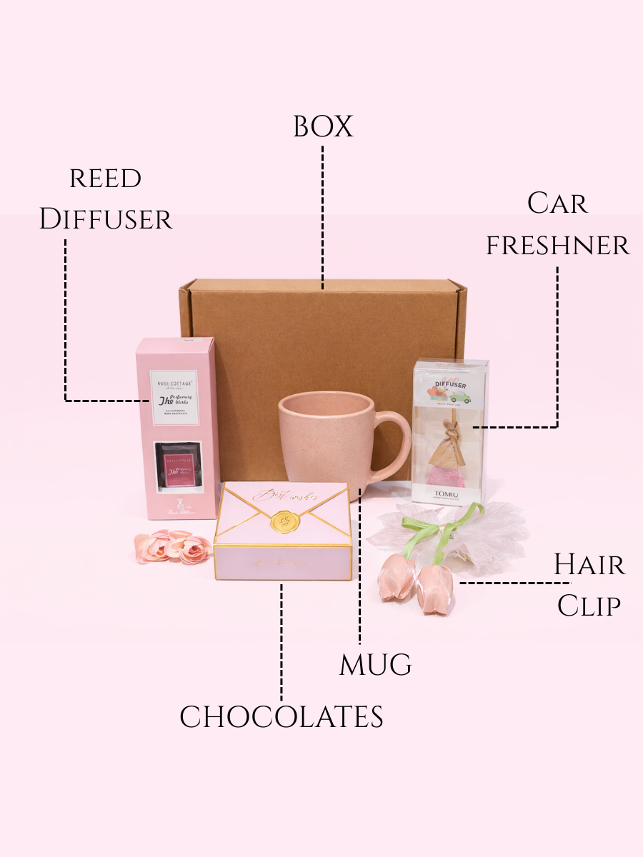 Gift set with reed diffuser, mug, chocolates, box, car freshener, and hair clip on a white background.