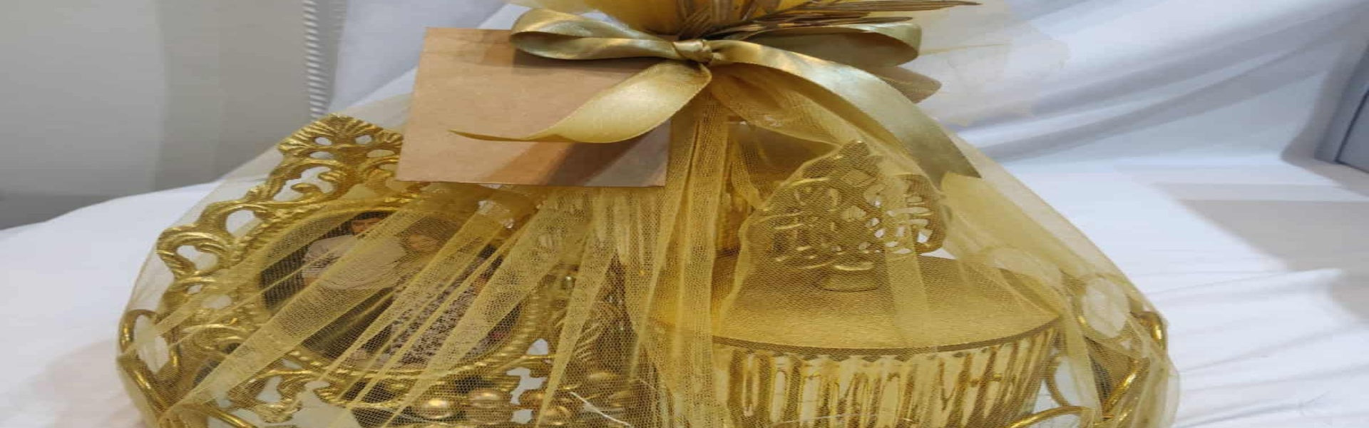 Gold gift basket with decorative bow on a white surface