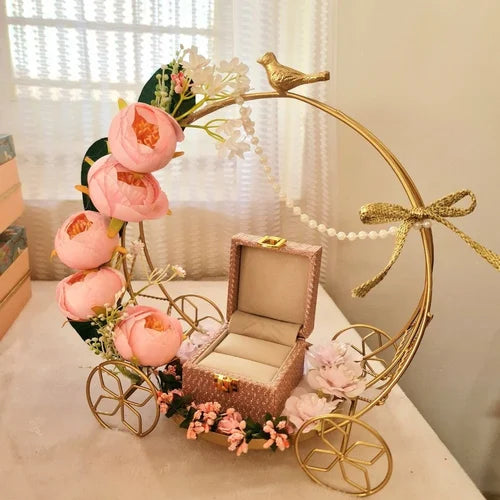 Decorative gold carriage with pink flowers and a jewelry box on a white surface.