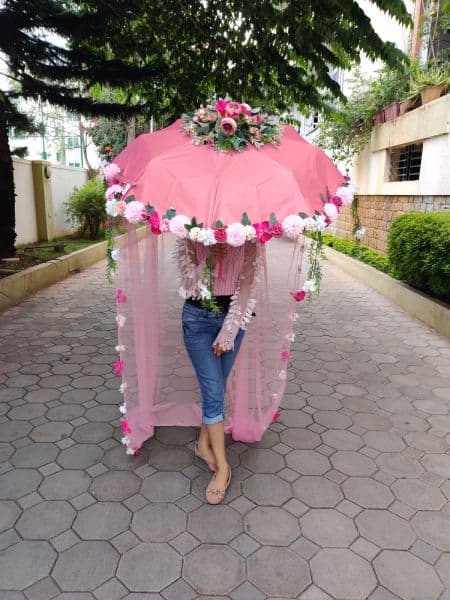 Person holding a large pink decorative umbrella with flowers on a paved walkway.