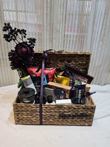 Gift basket with flowers, snacks, and a bottle of wine on a white surface.