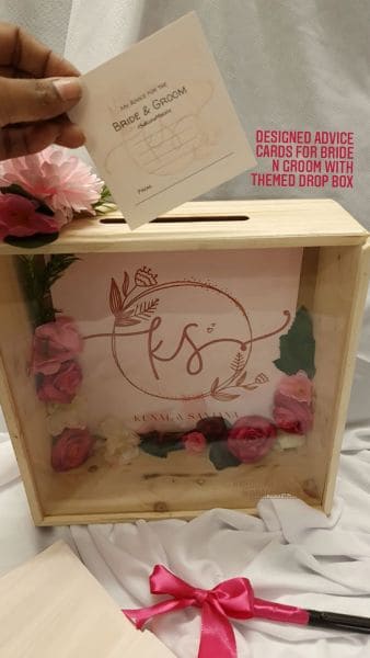 Wooden box with 'KS' logo, pink flowers, and a card being held above it.